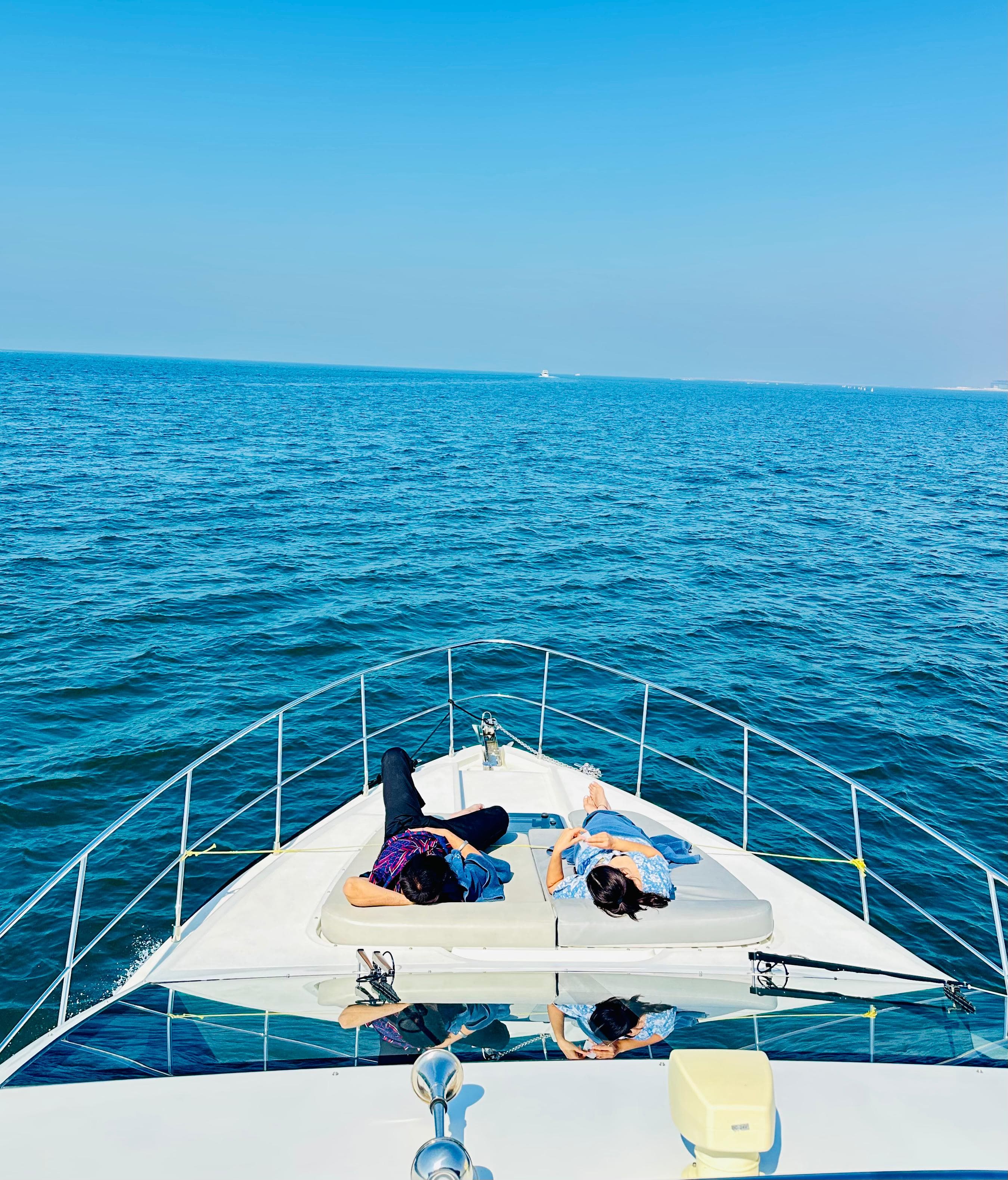 Couple relaxing on yacht bow sunpads cruising the open Arabian Gulf waters